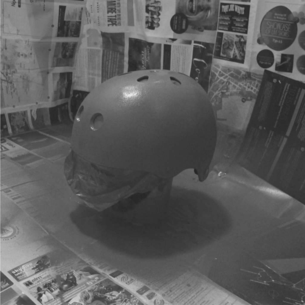 A roller skating helmet, stuffed with plastic bags, sat upon a yoghurt pot inside the newspaper protector. It has been sprayed with a grey primer.