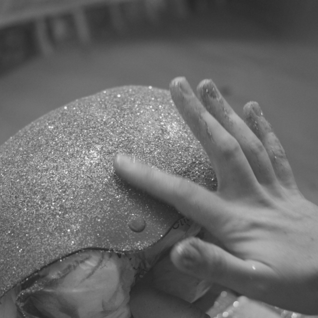 A hand holding a sparkly roller skating helmet, with the right hand gently rubbing the glitter.